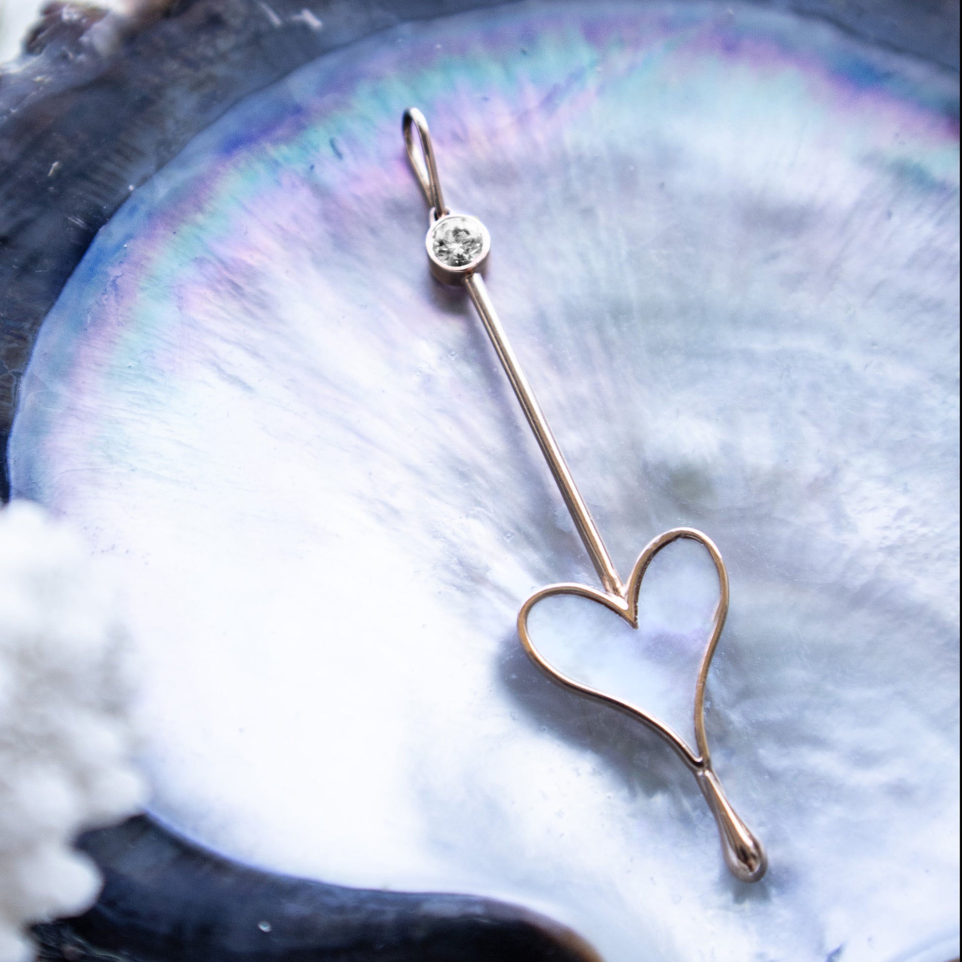Love Wand Pendant in 18k rose gold with luminous mother-of-pearl resting on a natural oyster shell