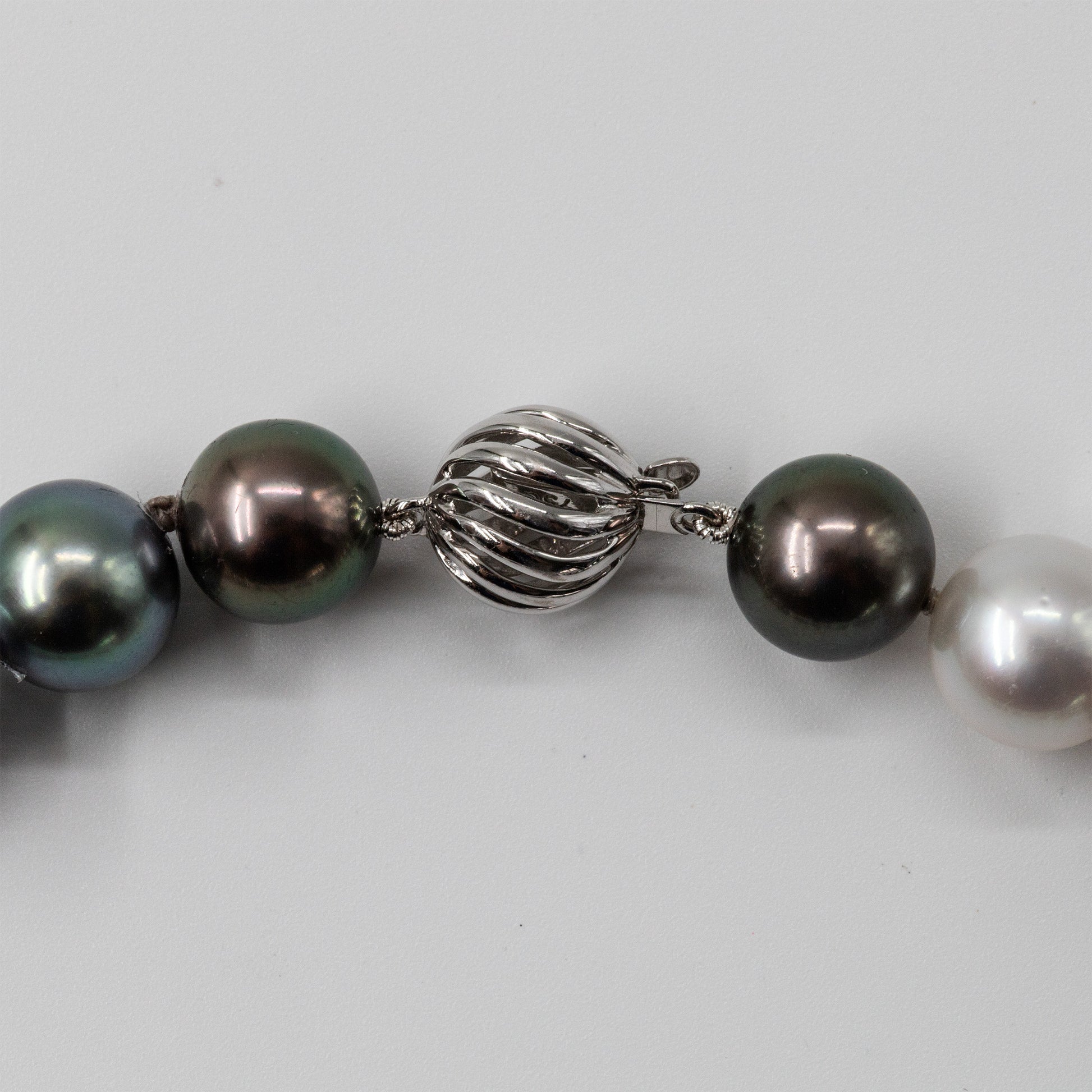 Cropped view of an 18k white gold swirl clasp on a Roseate multicolor necklace featuring genuine Tahitian and White South Sea cultured pearls with peacock, silver, charcoal, and white overtones