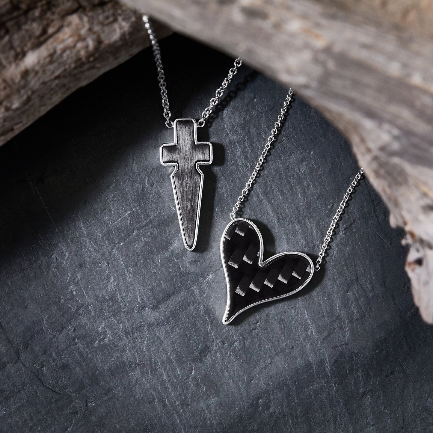 The Odyssey | Roseate Strength collection pendants in sterling silver and carbon fiber, styled with driftwood on slate.