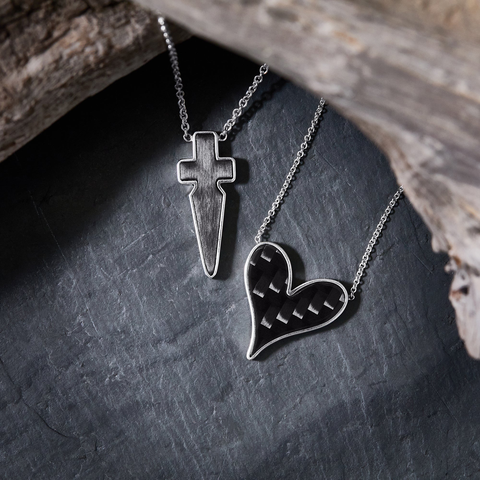 The Odyssey | Roseate Strength collection pendants in sterling silver and carbon fiber, styled with driftwood on slate.